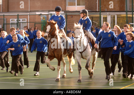 ZWEI SCHULMÄDCHEN AUF PFERDEN AUF EINEM SPIELPLATZ AN EINE JUNIOR SCHOOL SOMERSET UK Stockfoto