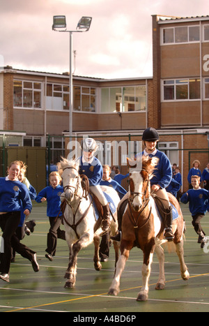 ZWEI SCHULMÄDCHEN AUF PFERDEN AUF EINEM SPIELPLATZ AN EINE JUNIOR SCHOOL SOMERSET UK Stockfoto