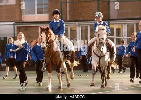 ZWEI SCHULMÄDCHEN AUF PFERDEN AUF EINEM SPIELPLATZ AN EINE JUNIOR SCHOOL SOMERSET UK Stockfoto