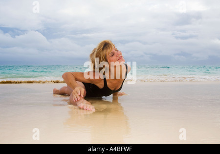 schöne 50 Jahre alte Frau beim Yoga am Strand Stockfoto