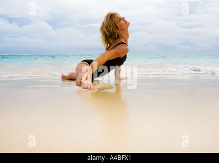 schöne 50 Jahre alte Frau beim Yoga am Strand Stockfoto