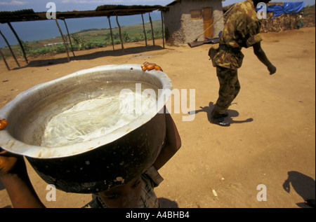 Kamenge Zusammenschluss Camp, Burundi Februar 2000: ein junges Mädchen führt das Wasser von einer Wasserstelle als eine Soldaten-Spaziergänge durch. Stockfoto