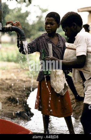 Zwei Kinder bekommen Wasser aus einem Hahn in der Landwirtschaftszone Grün in Maputo, Mosambik Stockfoto