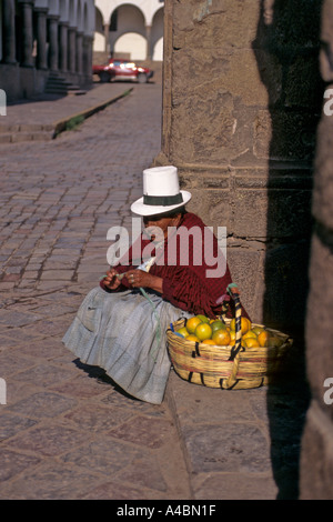 Cusco, Peru. Frau im traditionellen weißen Filzhut Orangen aus einem Korb auf der Ecke der Straße zu verkaufen. Stockfoto