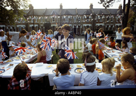 FAMILIEN & JUNGE KINDER PARTY ESSEN AUF GEMEINSAMEN RASEN AUßERHALB DER HÄUSER, FEIERT DIE KÖNIGLICHE HOCHZEIT IM JULI 1981. Stockfoto