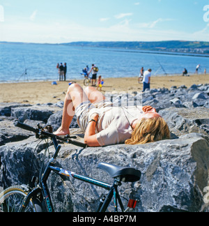 Eine Radfahrerin, die auf einem Felsen im Millennium Coastal Park bei Llanelli in Carmarthenshire liegt. Wales Coastal Path UK KATHY DEWITT Stockfoto