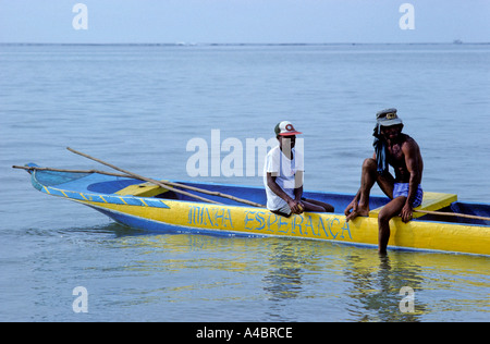 Insel Itaparica, Bahia, Brasilien. Zwei Fischer schauen entspannt in eine gelbe und gebläuten Einbaum Kanu "Minha Esperanca". Stockfoto