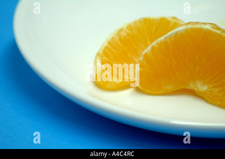 Zwei Segmente der orange Citrus Sinensis auf einem weißen Teller mit blauem Hintergrund Stockfoto