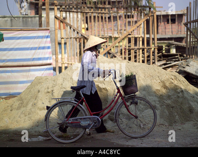 Mann mit Sand Pan Hut mit Fahrrad vor Buliding Website Vietnam, Asien Stockfoto