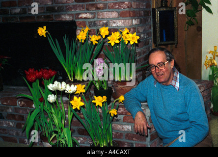 Junger Mann zeigt stolz auf Erfolg in wachsenden Tulpen und Narzissen in den Türen in Töpfen Stockfoto