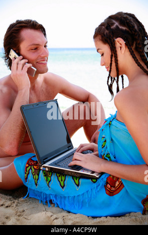 Junges Paar mit Laptop und Handy am Strand Stockfoto