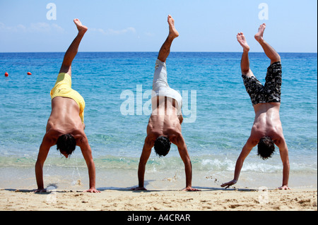 Drei junge Männer tun Handstand am Strand Stockfoto