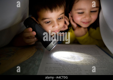 Jungen und Mädchen lesen ein Buch Taschenlampe unter der Bettwäsche Stockfoto