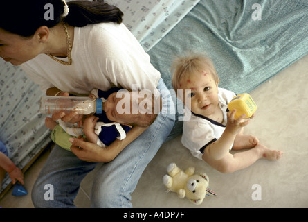 Ein Kleinkind spielt da die Tagesmutter ein Baby füttert. Die Kinderkrippe des Halles, Paris. Frankreich Stockfoto