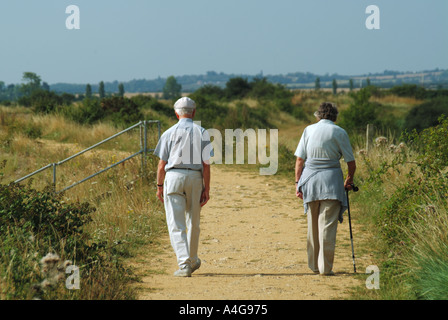 Rückansicht eines Paares, der auf einem Wanderweg in der ländlichen Landschaft neben dem Fluss Blackwater Lady mit dem Wanderstock Essex England UK spaziert Stockfoto