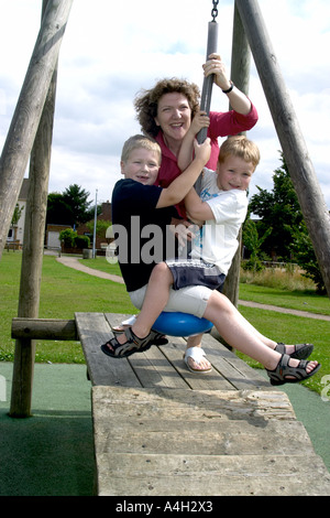 Eine Mutter mit ihren beiden Kindern auf einer Schaukel spielen. Stockfoto