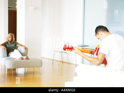 Mann spielt Gitarre, Rückansicht, Frau im Sessel sitzen Stockfoto