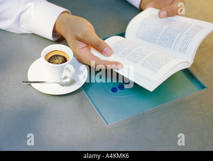 Hände des Mannes hält Buch neben Tasse espresso Stockfoto