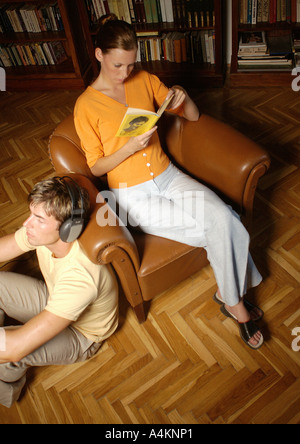 Mann mit Kopfhörern, Frau im Sessel, ein Buch zu lesen Stockfoto