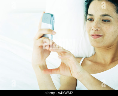 Frau liegend auf den Rücken zu Bett, Blick auf Handy Stockfoto
