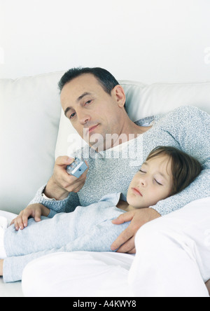 Mann sitzt auf der Couch zeigt Fernbedienung, schlafende Tochter auf Schoß hielt Stockfoto