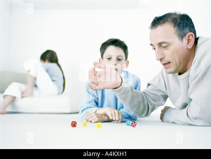 Mann und Sohn beim Würfelspiel auf Boden, Mädchen sitzen im Hintergrund Stockfoto