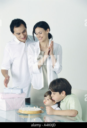 Mädchen und jungen Ausblasen der Kerzen auf Kuchen, Eltern stehen, beobachten Stockfoto