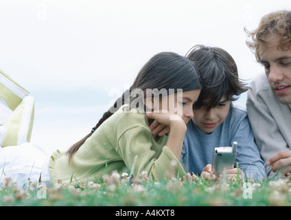 Jungen und Mädchen mit Vater liegend auf Bauch auf Rasen Blick auf Handy Stockfoto