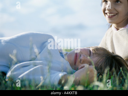 Junge liegend auf dem Rasen mit geschlossenen Augen, Mädchen hinter ihm Stockfoto