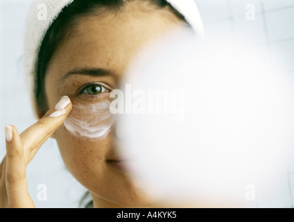 Frau, die Anwendung der Feuchtigkeitscreme unter Auge, verschwommene kompakt im Vordergrund Stockfoto