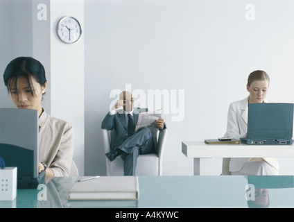 Zwei Frauen, die Arbeiten am Laptop im Büro, Geschäftsmann, sitzen im Stuhl und Las Zeitung im Hintergrund Stockfoto