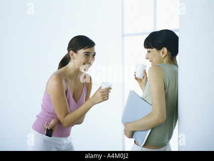 Zwei Frauen stehen mit Tassen, lachen Stockfoto