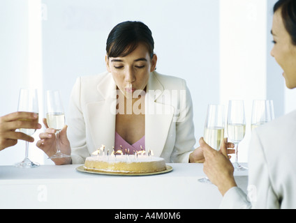 Frau Ausblasen der Kerzen auf Kuchen, sitzen zusammen mit anderen Menschen, hält Gläser Champagner Stockfoto