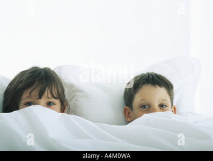 Jungen und Mädchen im Bett liegend, teilweise durch Bettdecke verdeckten Gesichtern Stockfoto