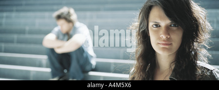 Junge Frau, Blick in die Kamera, junger Mann sitzt im Hintergrund Stockfoto