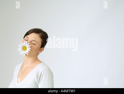 Junge Frau mit Blume im Mund und geschlossenen Augen, Porträt Stockfoto