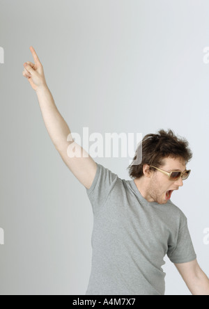 Junger Mann mit Hand oben in der Luft und Mund offen, Sonnenbrille, Porträt Stockfoto