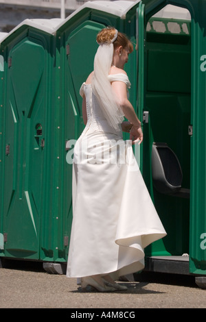 Eine Braut in einem weißen Kleid und Schleier, eine tragbare Toilette betreten. Stockfoto