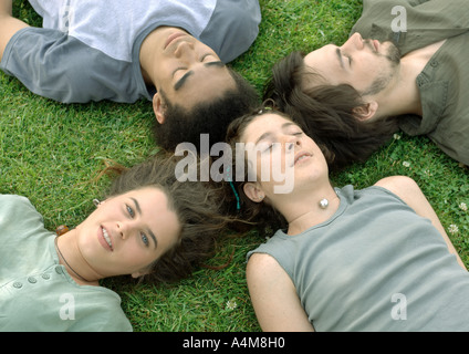 Vier Freunde liegen auf dem Rasen mit Köpfen zusammen Stockfoto