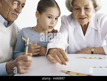 Großeltern und Mädchen sitzen am Tisch spielen holen Stöcke Stockfoto