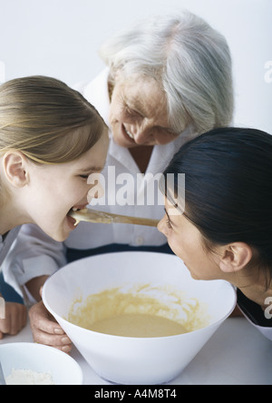 Großmutter mit Enkelinnen, ein Mädchen Verkostung Teig backen Stockfoto