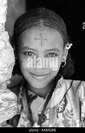 S/W-Porträt eines lächelnden Mädchens mit flüssigen Augen, traditioneller Frisur und einem koptischen christlichen Kreuz auf der Stirn. Adua, Äthiopien, Afrika Stockfoto