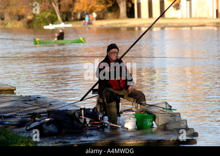 Ein Fischer auf der Seite der Isis, die Themse in Oxford an einem hellen Wintertag. Teilnahme an einem Kurs Angelwettbewerb Stockfoto