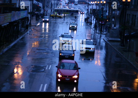 Autos fahren durch eine belebte Kreuzung an einem Regen und nassen Nacht auf der Randolph Street, Downtown Chicago, IL USA Stockfoto