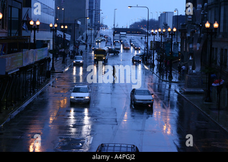 Man überquert Autos fahren durch eine belebte Kreuzung an einem Regen und nassen Nacht auf der Randolph Street, Downtown Chicago, IL USA Stockfoto