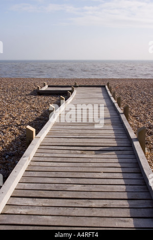 Ein Holzsteg führt über den Kiesstrand in Richtung Meer bei Dungeness vertikale Stockfoto