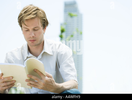 Junger Mann Lesebuch, Hochhaus im Hintergrund Stockfoto