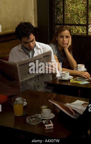 Mann liest eine Zeitung als gelangweilte Freundin neben ihm im Café sitzt Stockfoto