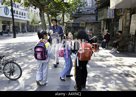 CHINA WUHAN drei junge chinesische Schulmädchen auf dem Heimweg von der Schule spielen, um gemeinsam auf dem Bürgersteig an einer belebten Straße Stockfoto