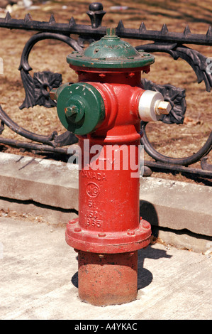 Rot bemalte Hydranten gegen Schmiedeeisen Zaun im historischen Viertel von Fredericton New Brunswick, Kanada Stockfoto